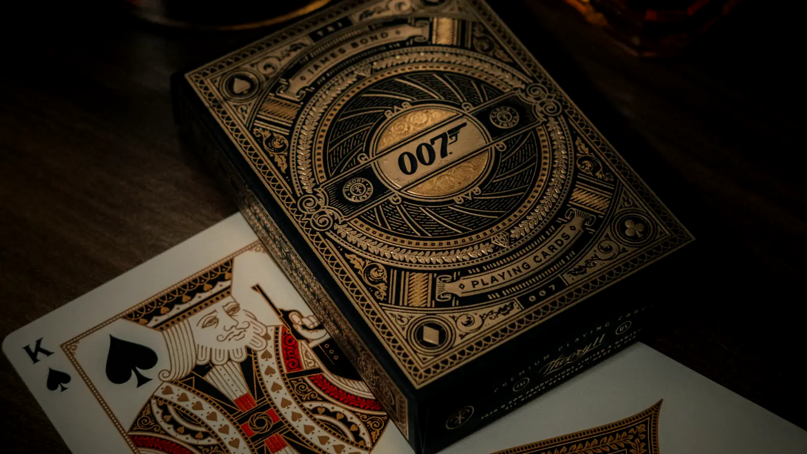 An ornate gold-and-black James Bond 007 playing-card deck beside a King of Spades card, on a dark table