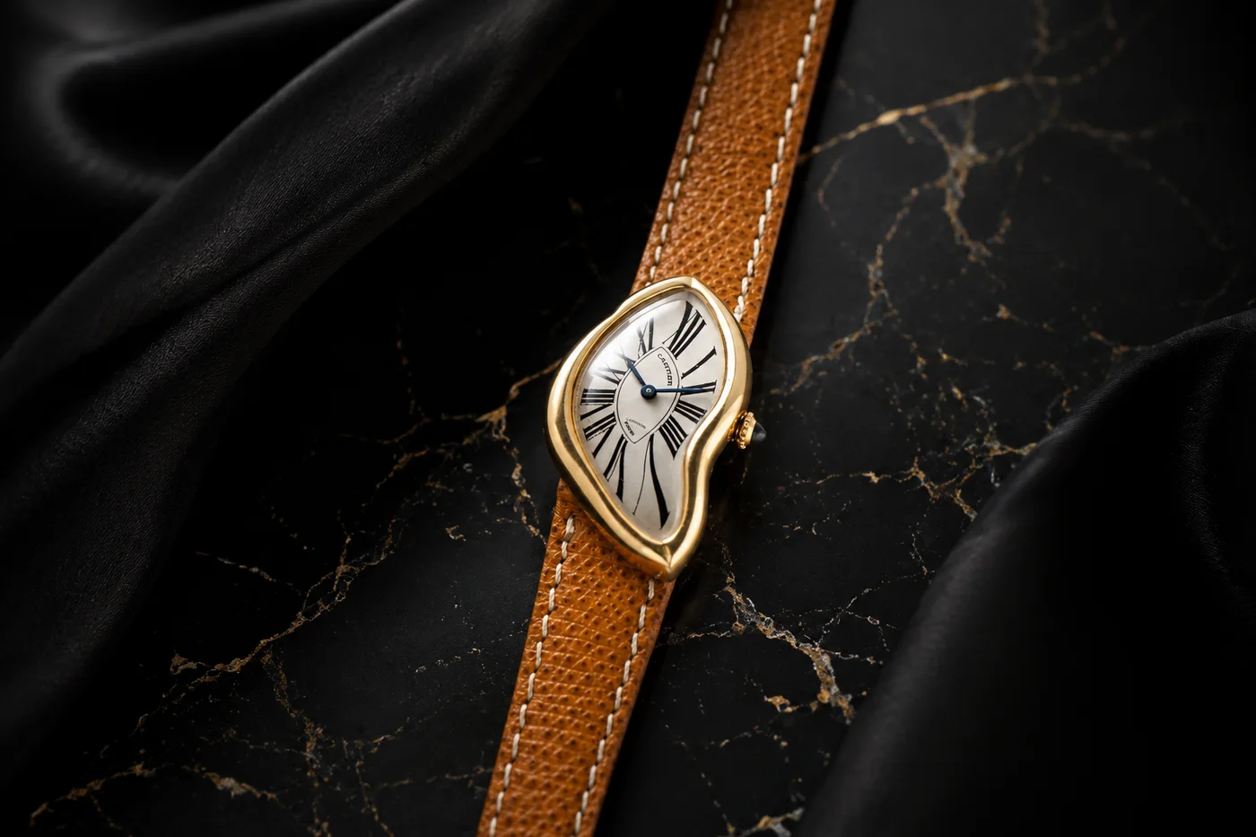 The Cartier Crash — a gold wristwatch with a deliberately distorted, melted-looking case and stretched Roman numerals, on a tan leather strap over black marble
