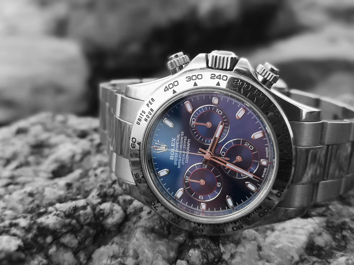 Rolex Cosmograph Daytona chronograph with a blue dial, resting on a stone surface