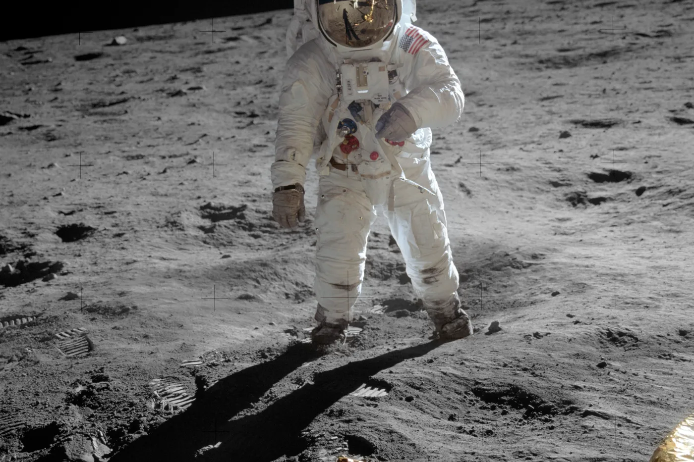Buzz Aldrin standing on the Moon during Apollo 11, Neil Armstrong and the lunar module reflected in his gold visor, his Omega Speedmaster worn over the spacesuit