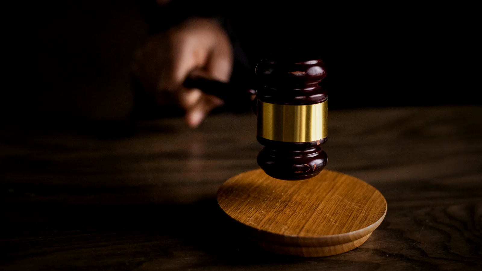 A gold-banded auctioneer's gavel coming down on its wooden block in dramatic low light — the hammer falling on a sale