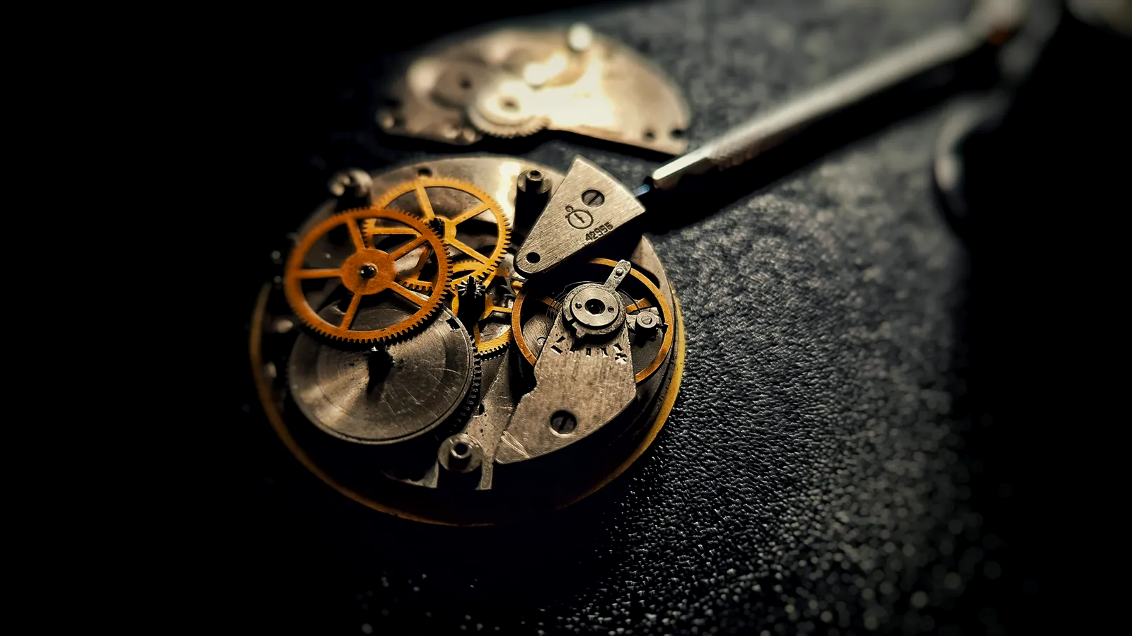 A macro of a mechanical watch movement — gold gears, mainspring and a watchmaker's tool in dramatic light, the craft the GPHG celebrates