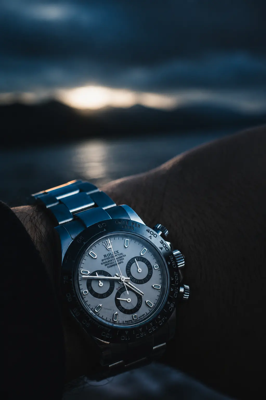 A steel Rolex Cosmograph Daytona with a black bezel on a rubber strap, worn at dusk