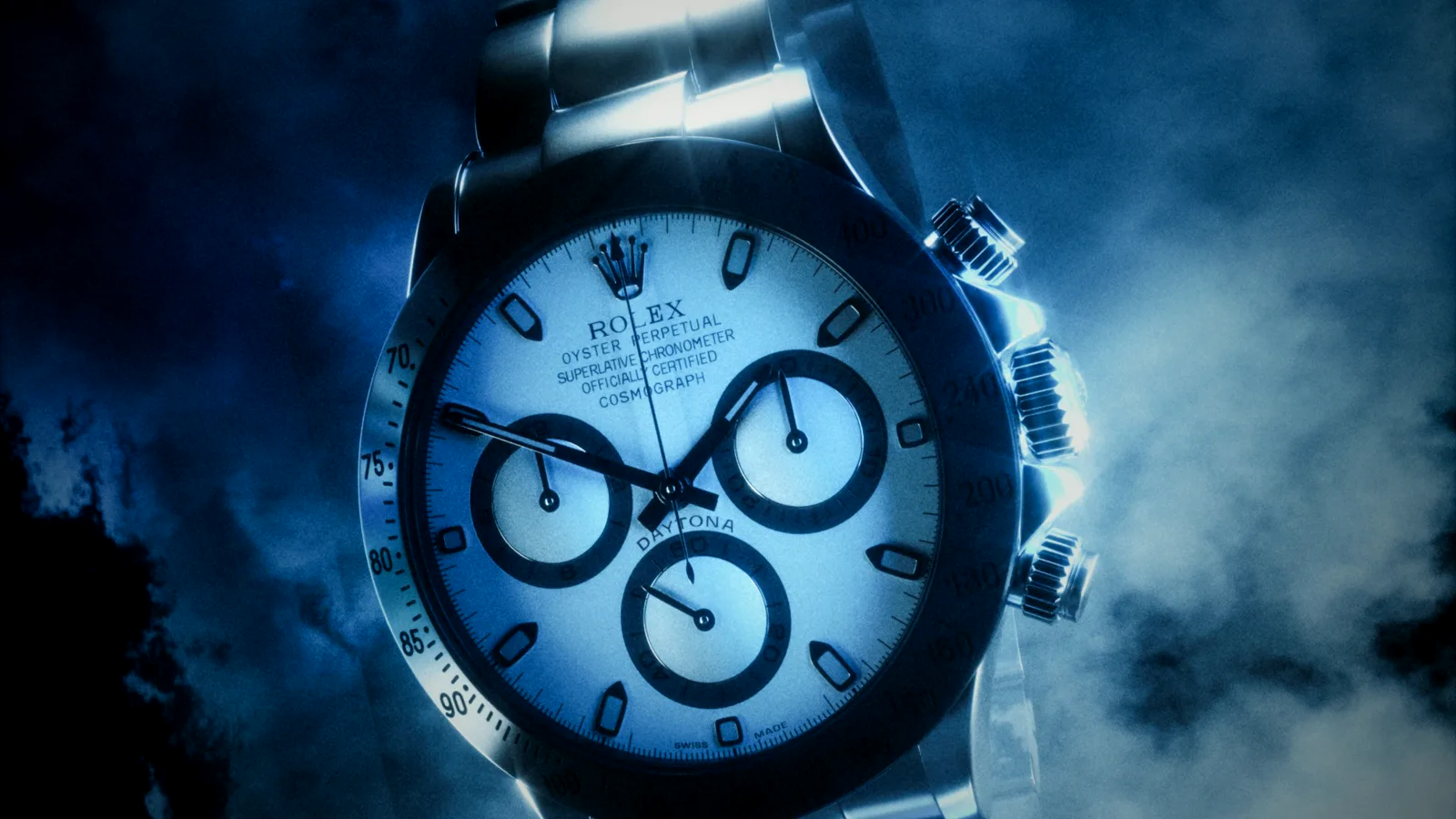 A steel Rolex Cosmograph Daytona with a white dial, lit dramatically in blue smoke against a dark sky — the kind of grail that defines a serious collection