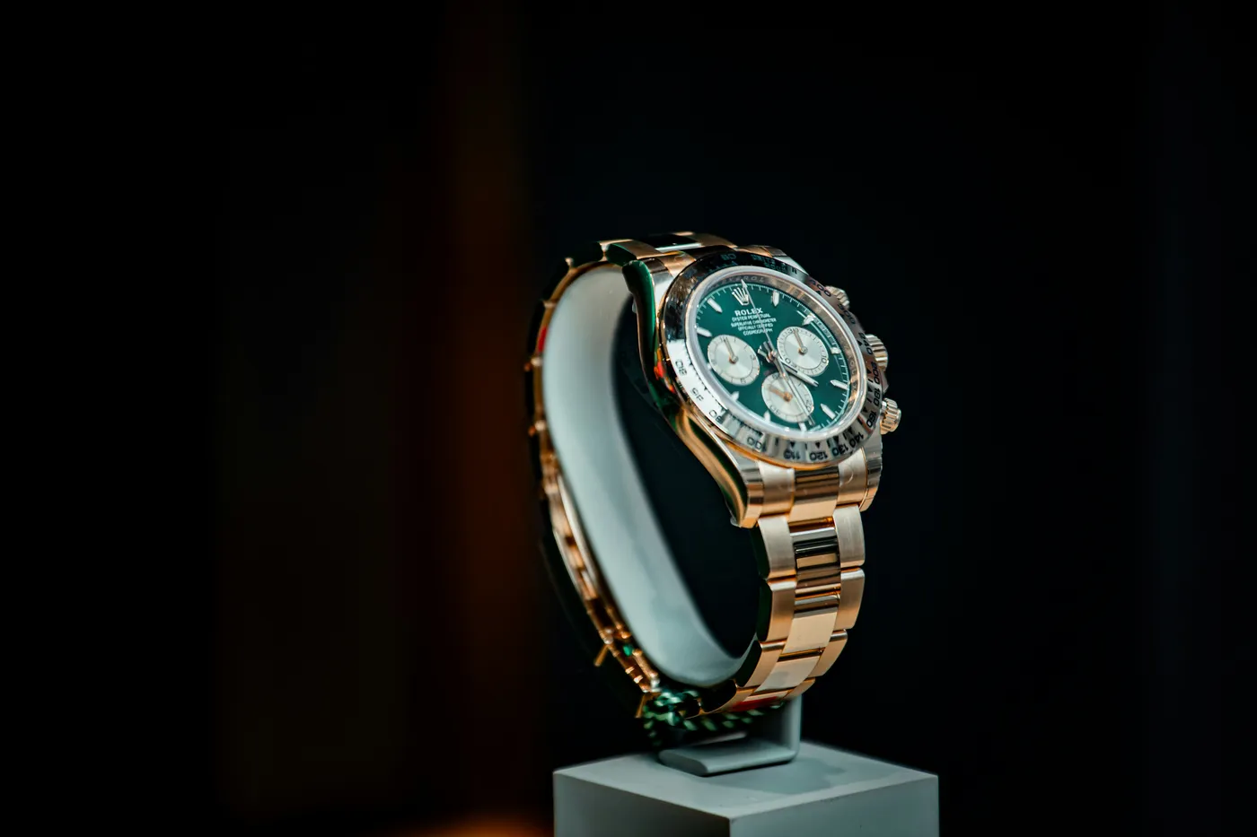 A gold Rolex Cosmograph Daytona with a green dial and white subdials, photographed on a dark background