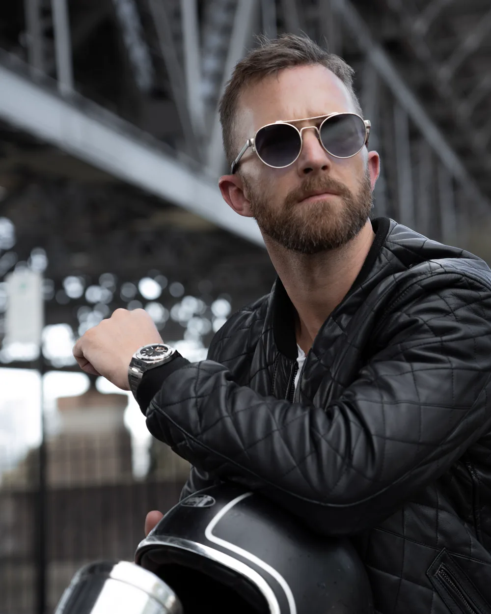 A composed, bearded man in aviator sunglasses and a leather jacket, a chronograph on his wrist — the modern heir to the test-pilot, astronaut spirit the Speedmaster was built for