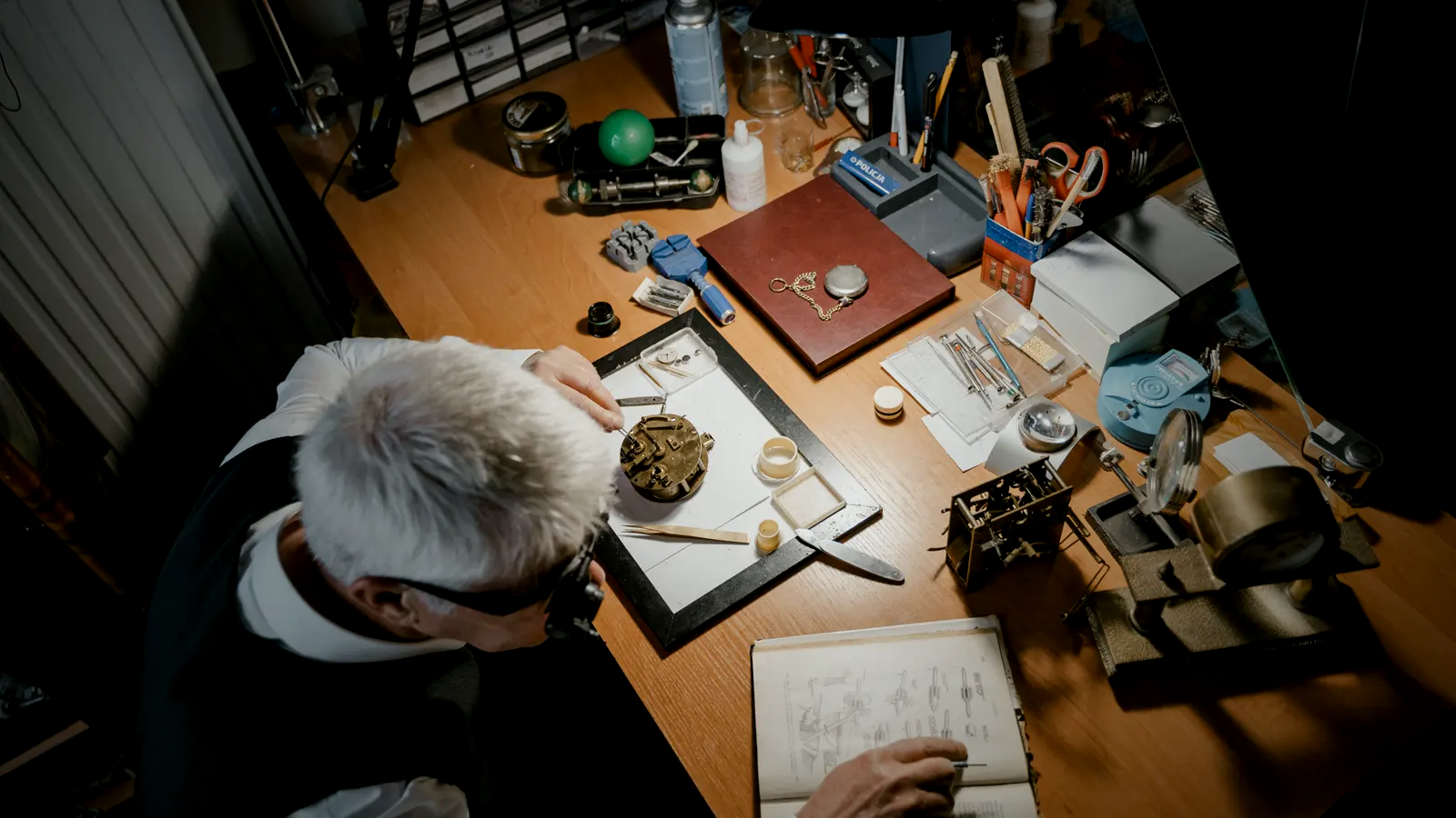 A watchmaker at his bench, loupe in place, working on a mechanical movement — the craft of building a calibre in-house