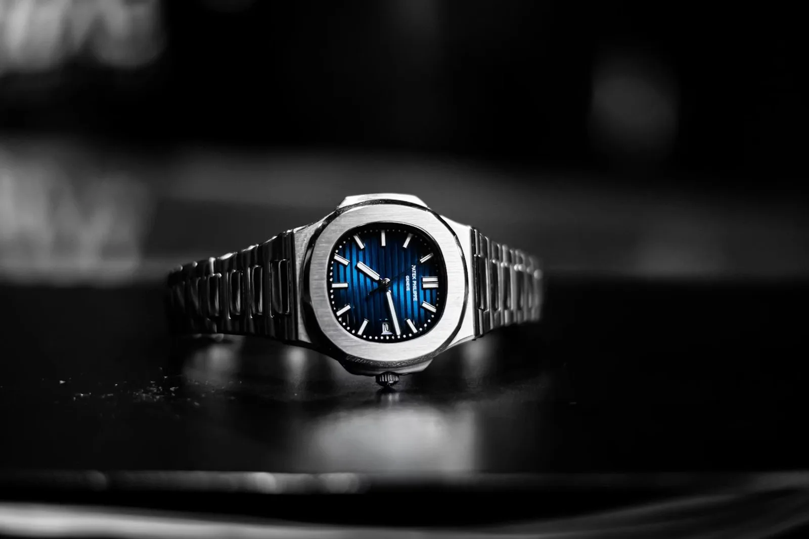 A stainless-steel Patek Philippe Nautilus with its embossed blue dial and integrated bracelet, on a dark reflective surface