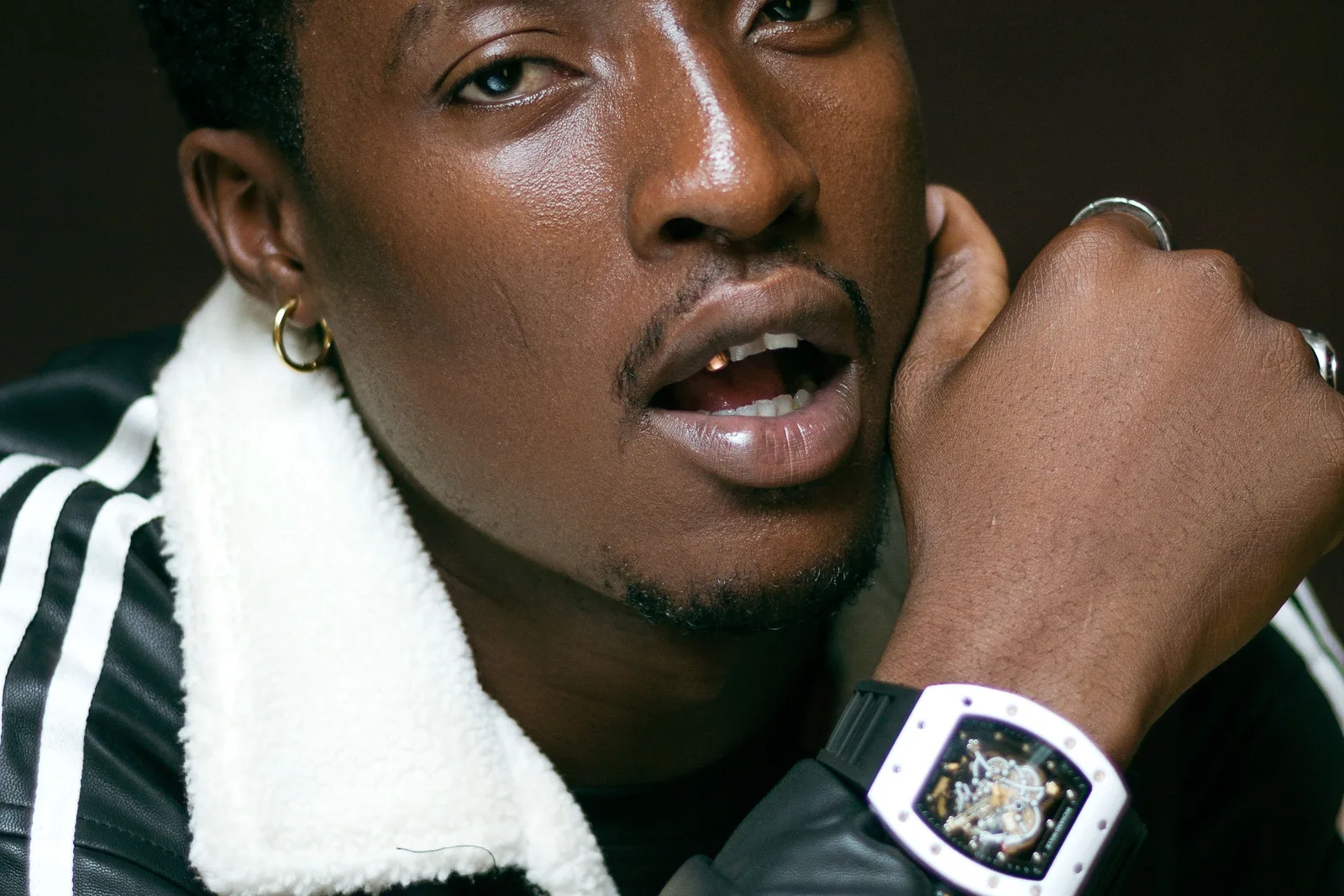 A man wearing a white Richard Mille tonneau watch with a skeletonised dial, hand raised to his face