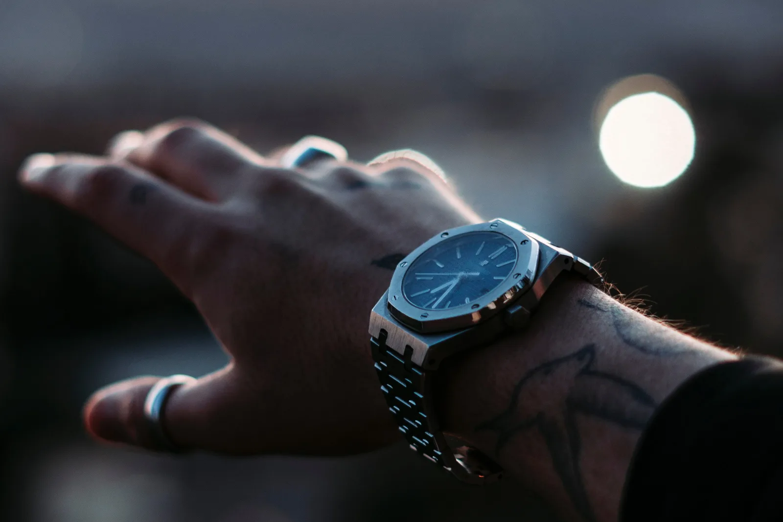 A stainless-steel Audemars Piguet Royal Oak with a blue dial and integrated bracelet, worn on the wrist at dusk